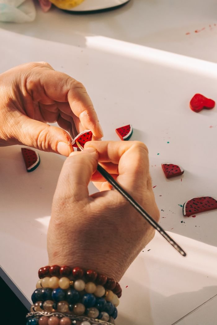 Hands skillfully crafting tiny polymer clay watermelons on a table in natural light.