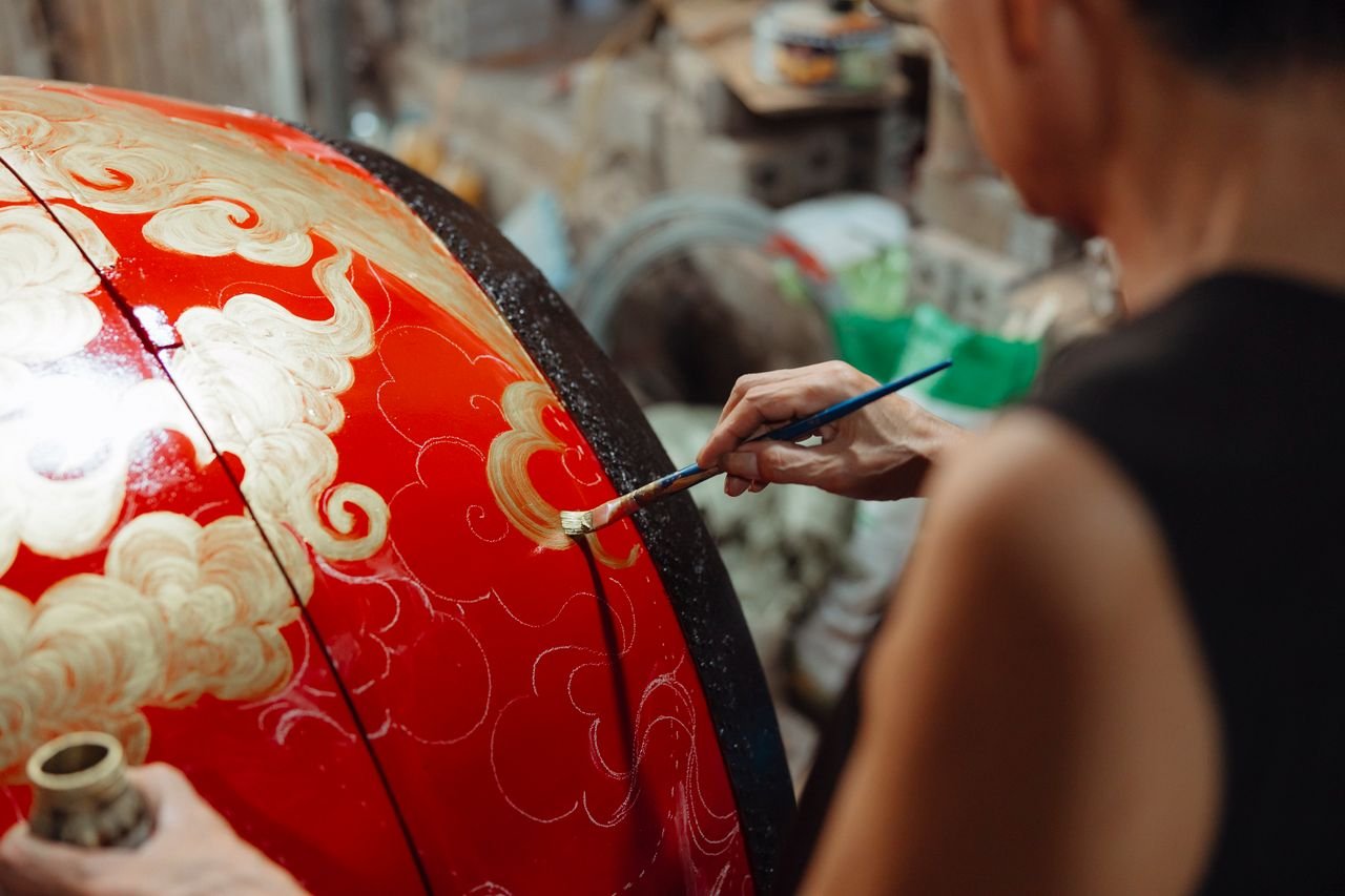 Close-up of an artisan painting intricate patterns on a large red spherical object, showcasing traditional craftsmanship.